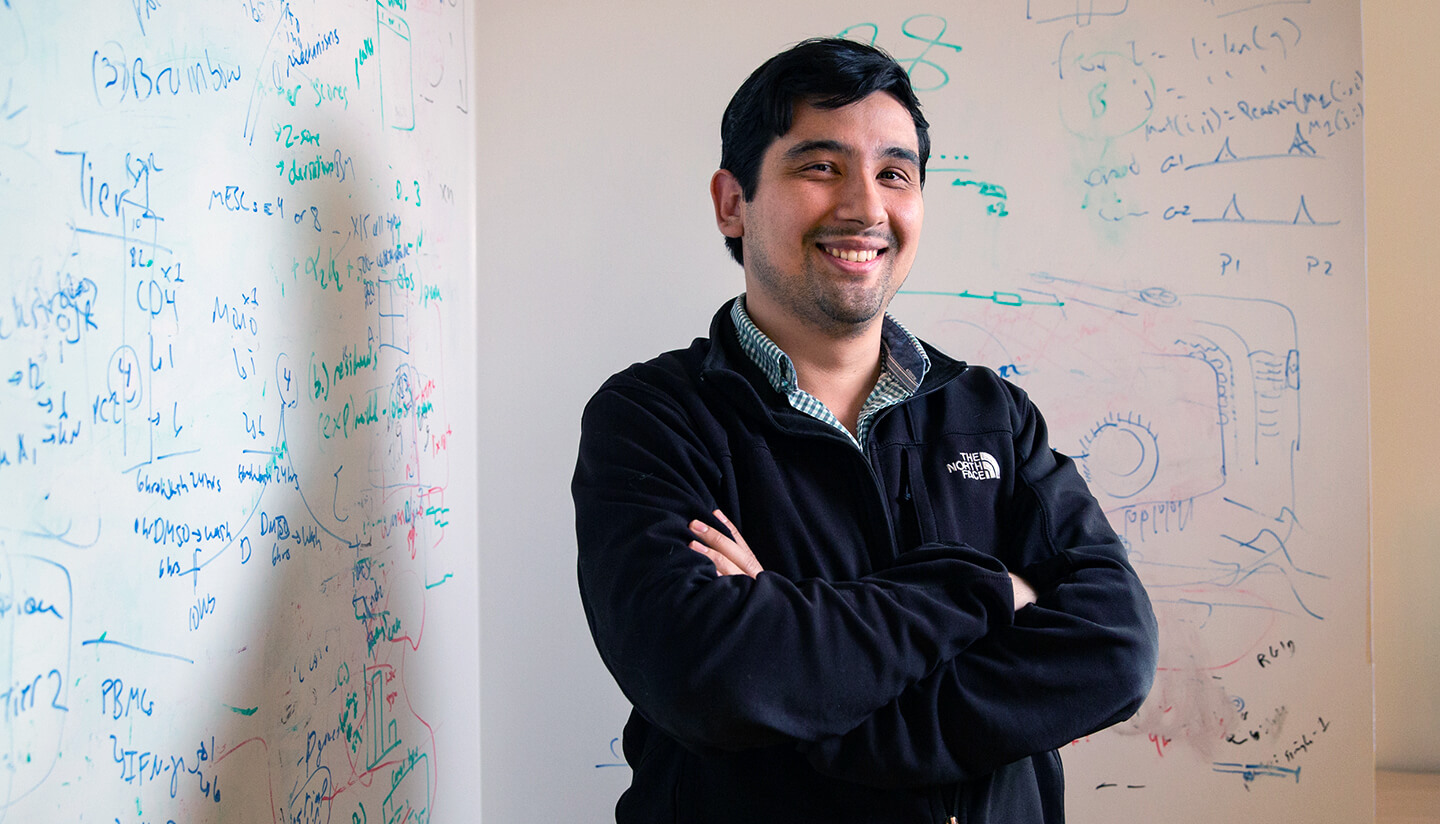 Photo of Jason Buenrostro with arms folded, smiling, in front of a white board with equations written on it