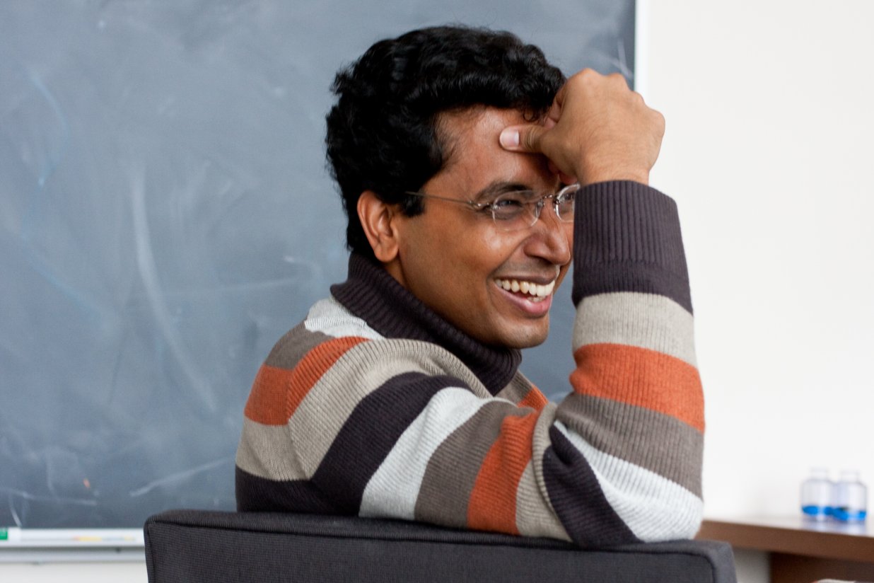 Sharad Ramanathan sitting in front of a chalkboard, laughing