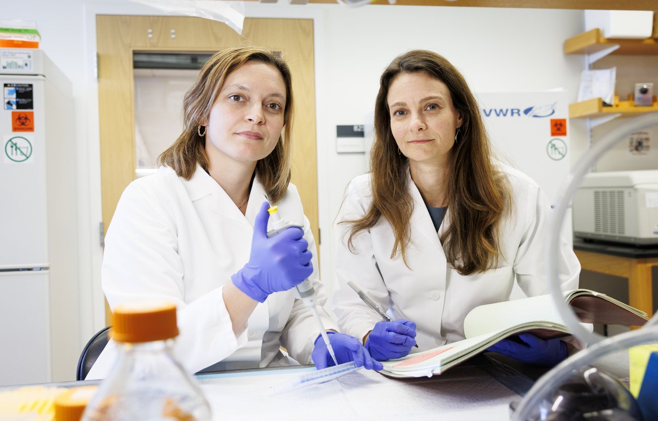 Daisy Hoagland (left) and Ruth Franklin working in the lab in lab coats, one with a pipette.